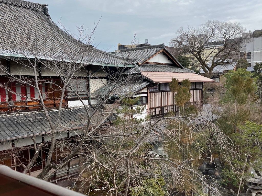 這張照片展現的是祇園花街藝術資料館庭園外觀的一隅，鏡頭從建築二樓俯瞰整個傳統日式建築群與庭園，四周環繞著冬日枯枝與靜謐氣息，充滿古都風韻。