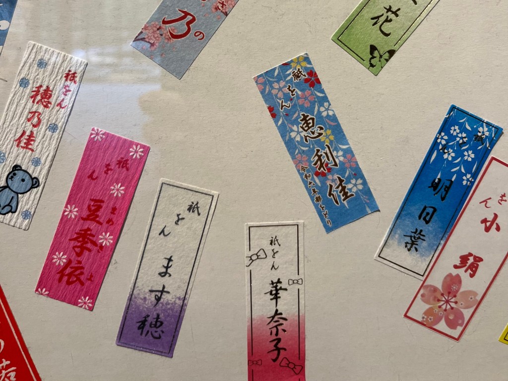 這張照片拍攝的是**千社札（せんじゃふだ）**的展示，這些色彩繽紛的長條紙牌上印有舞妓們的藝名，是祇園文化中非常有趣又富人情味的小物，具有高度辨識性與收藏價值。