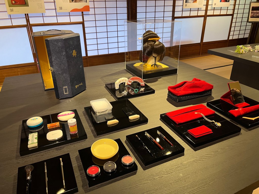 京都祇園花街藝術資料館中展示的舞妓化妝與梳妝工具，包括白粉、刷具、唇彩、鏡子與假髮等完整化妝組合