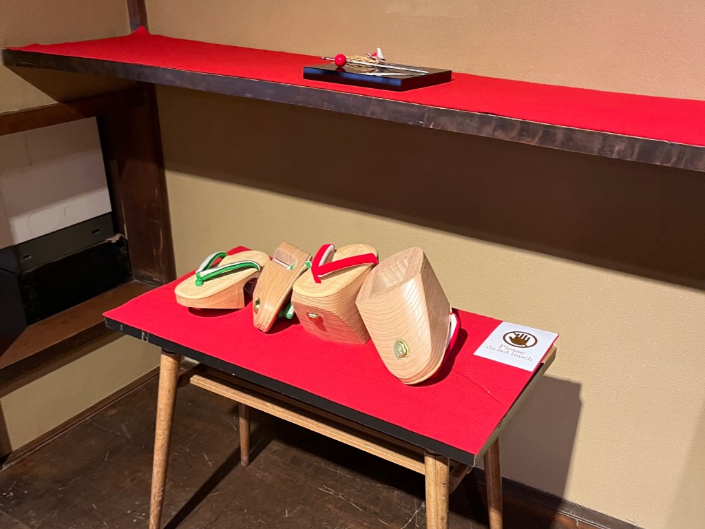 祇園花街藝術資料館展示的舞妓木屐，下方為紅布展示台，上排為不同款式的傳統木製下駄與岡足袋。
